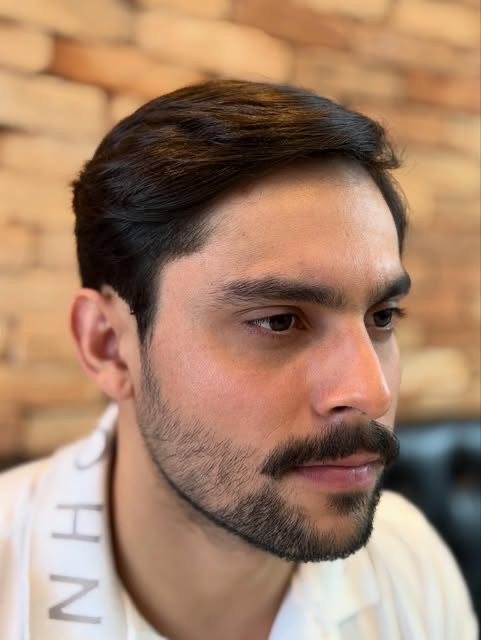 Cliente com corte social e barba desenhada na parede de tijolinhos da barbearia